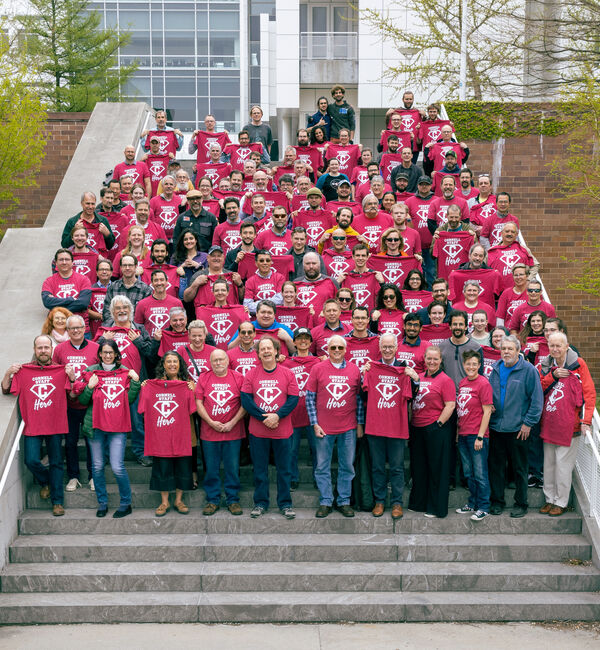 About 100 CLASSE staff lined up on s set of stairs wearing their red cornell heros t-shirt.